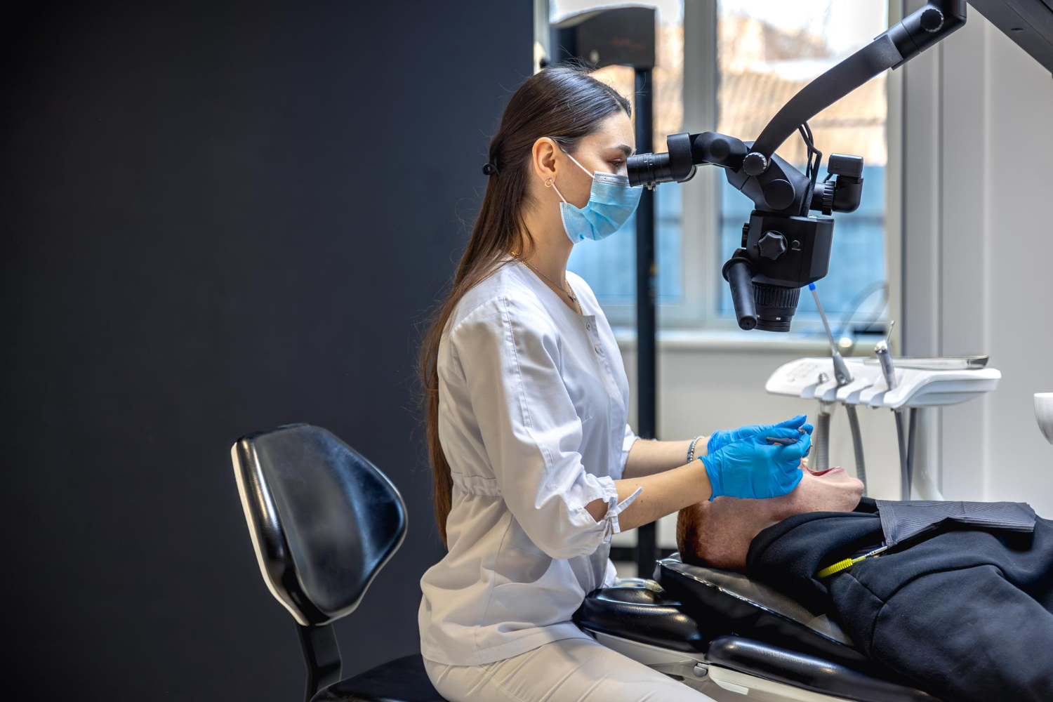 Jeune dentiste utilisant un microscope dentaire pour soigner un patient