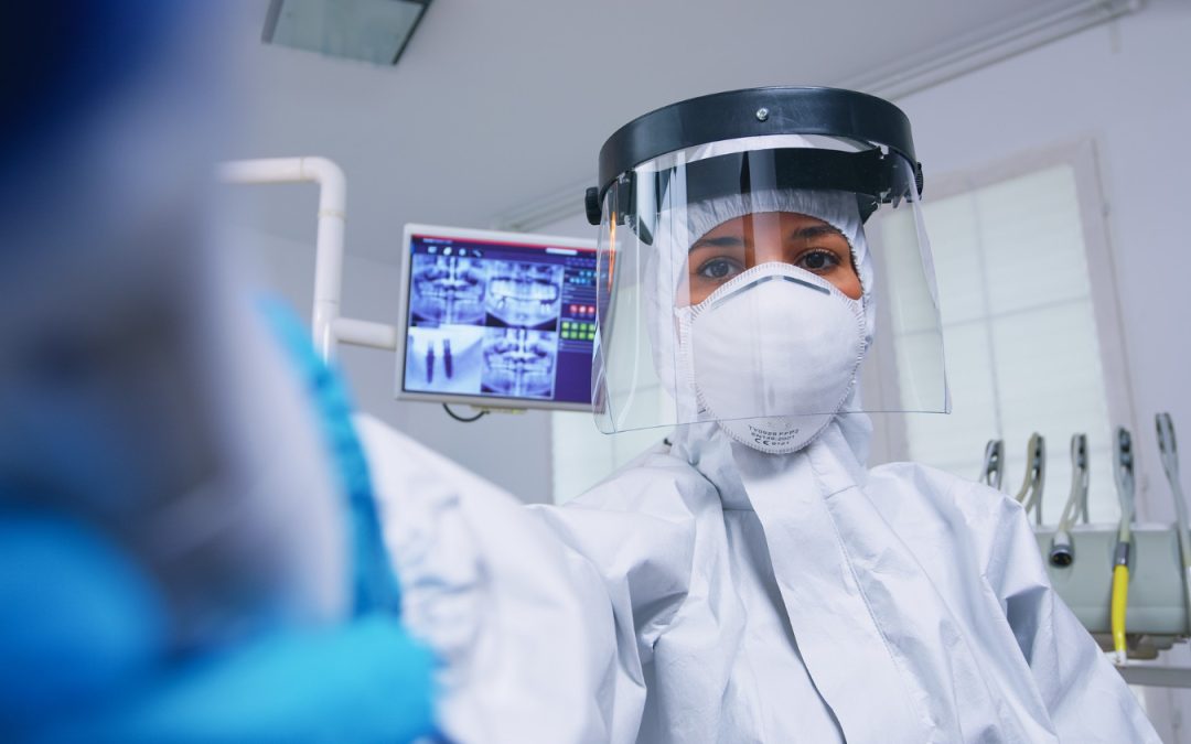 ne dentiste équipée d'une tenue de protection intégrale, À l'arrière-plan, un écran affiche des radiographies numériques